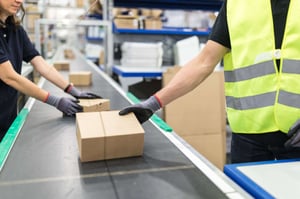 Close-up of workers’ gloved hands checking boxes on a conveyor belt