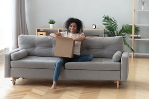 Smiling woman opening a box while seated on her couch