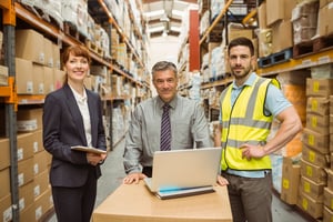3 business people at a laptop in a fulfillment warehouse