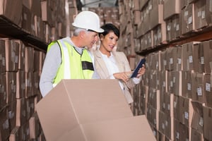 Warehouse worker moving boxes on trolley talking to manager in a large warehouse