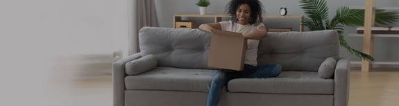  Woman smiling as she opens a box while seated on her couch