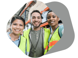 Three smiling employees in yellow safety vests with warehouse shelves behind them