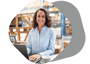Smiling woman at a desk with boxes in a warehouse behind her